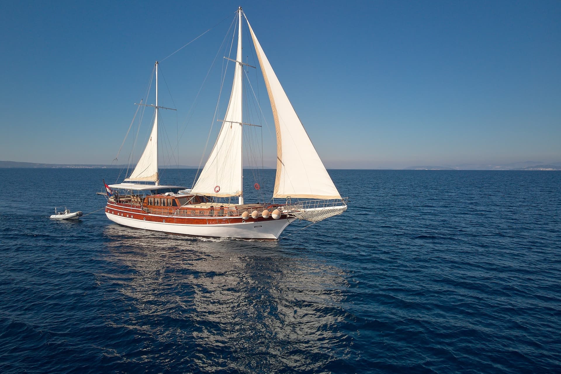 Wooden sailboat with white sails on deep blue Adriatic waters near a distant coastline.