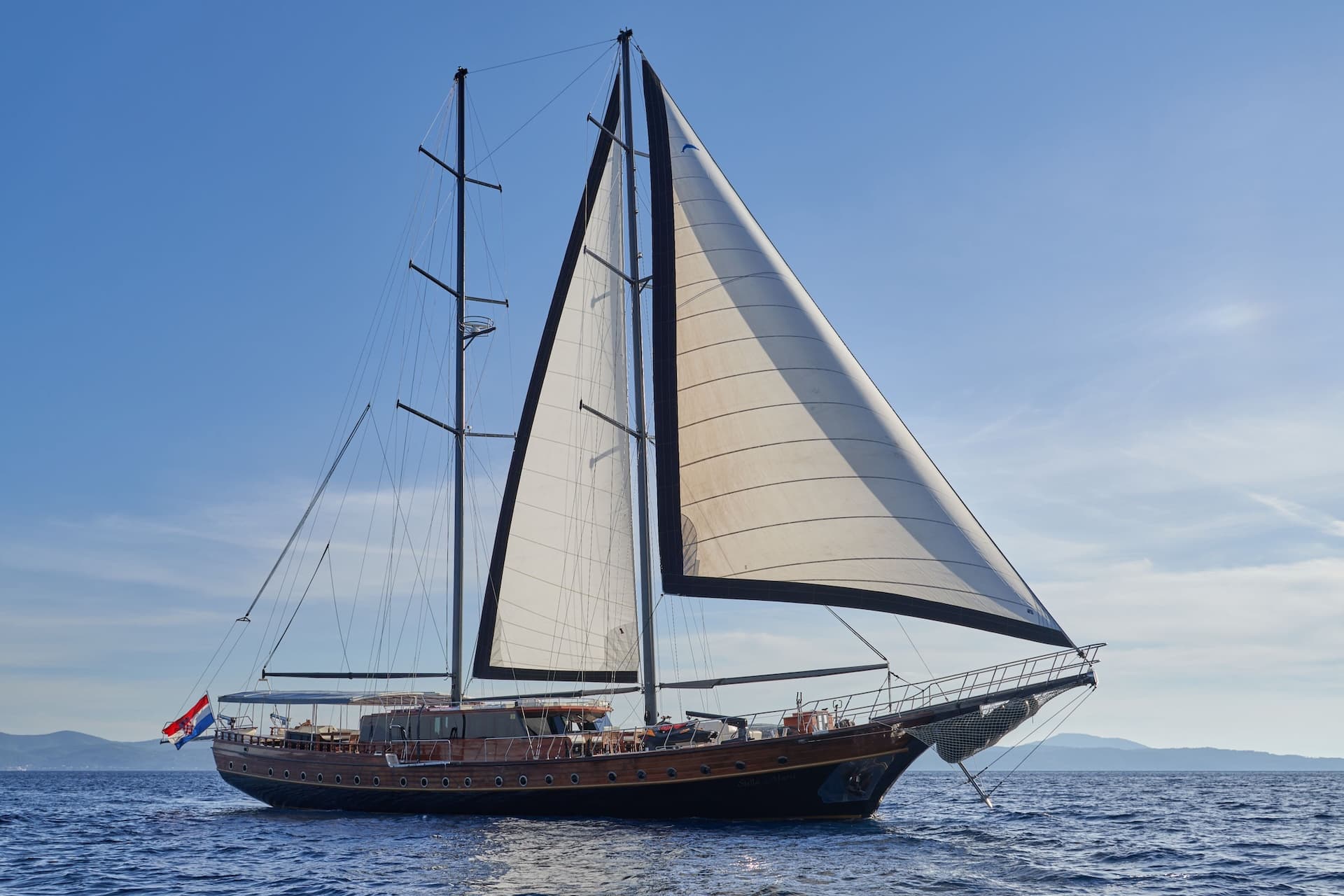 Wooden sailboat Stella Maris with sails up on blue sea near distant coastline