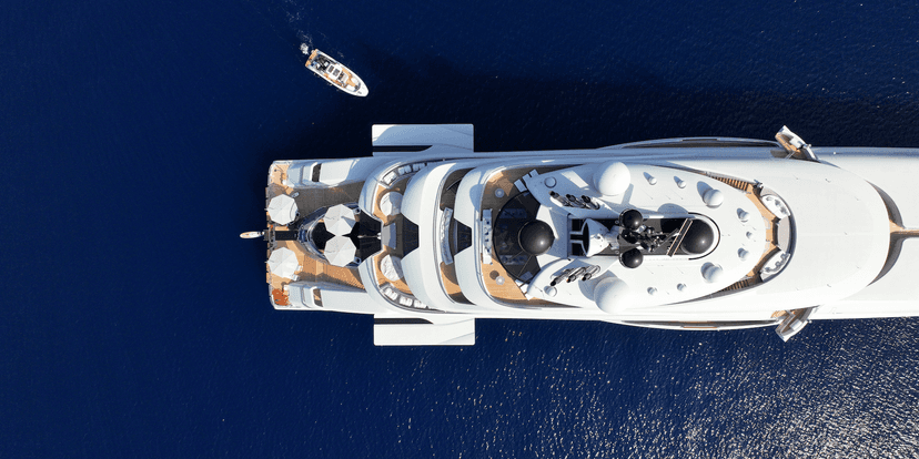 Aerial view of a large white luxury yacht on deep blue water near a small tender boat.